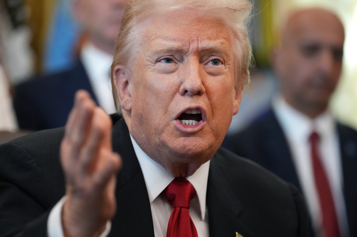 男性がスーツとネクタイを着て話している様子。背景に他の人がいる。