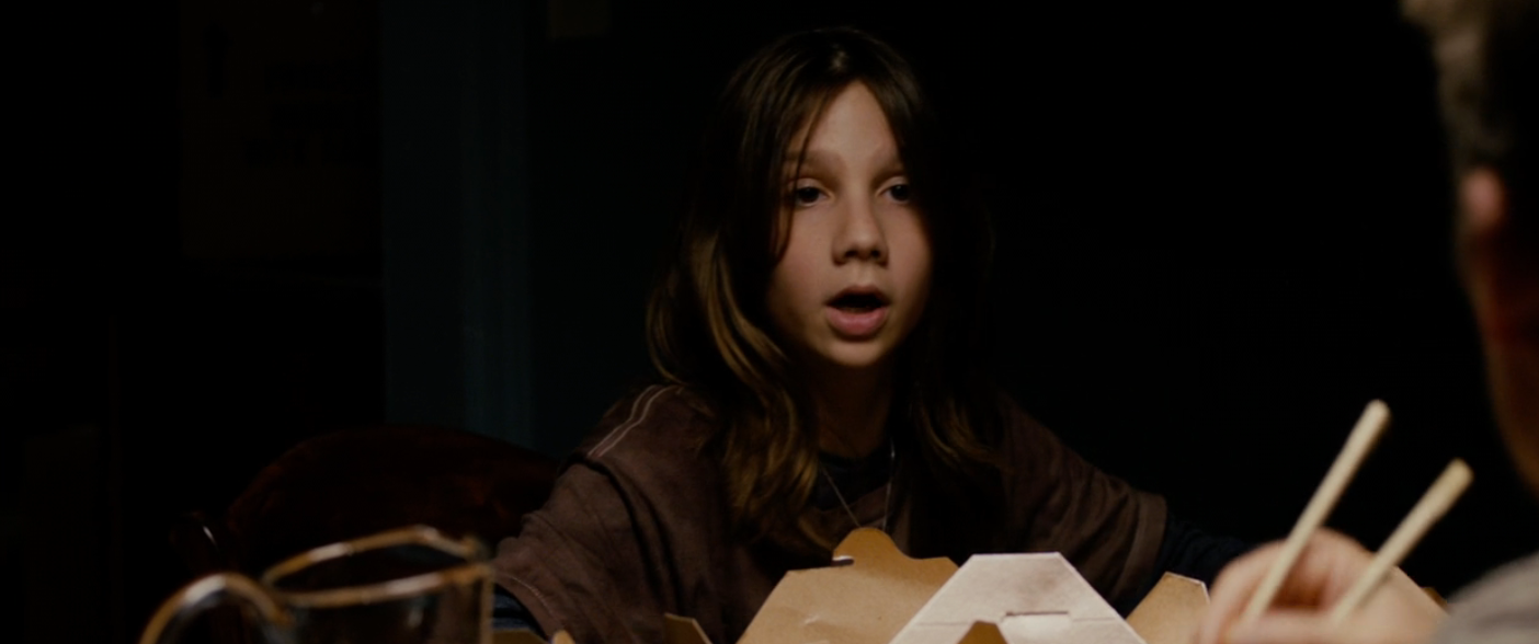 A kid  sits astatine  a table, surrounded by takeout boxes, talking to an unseen idiosyncratic   off-camera successful  a dimly lit setting