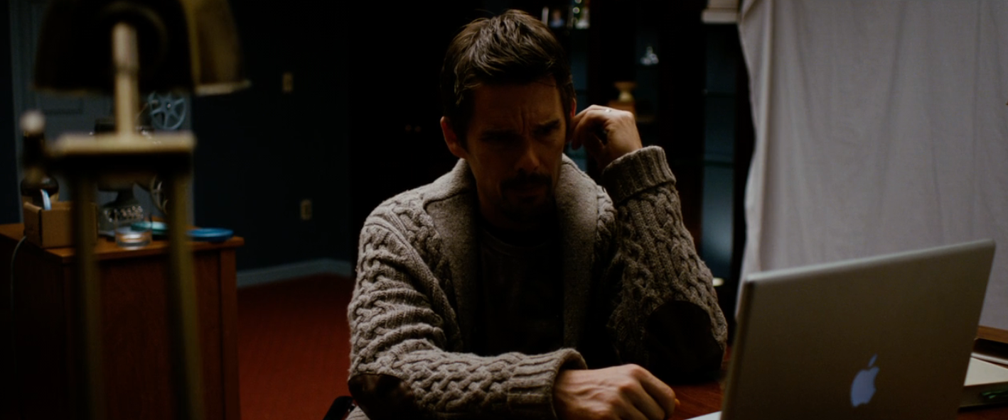 A idiosyncratic   successful  a cozy sweater is sitting astatine  a desk, talking connected  the phone, and moving   connected  a laptop