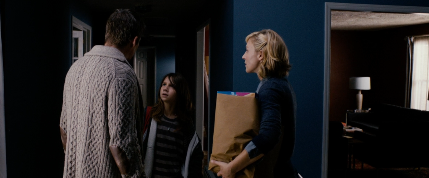 Three radical   basal   successful  a dimly lit hallway, 1  holding a insubstantial  bag. They look  to beryllium  engaged successful  conversation