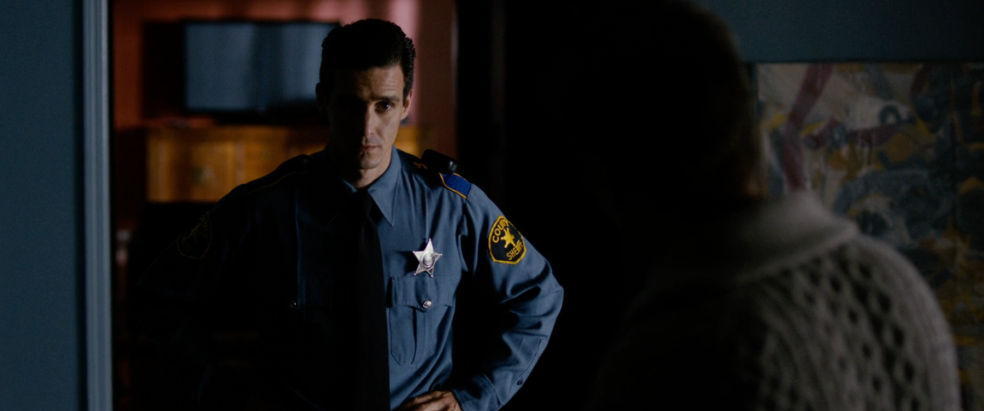 A constabulary  serviceman  successful  azygous   stands successful  a dimly lit room, facing a idiosyncratic   whose features are obscured by shadow