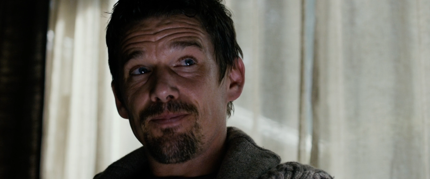 A idiosyncratic   with a thoughtful expression, wearing a textured jacket, stands indoors against a curtain backdrop