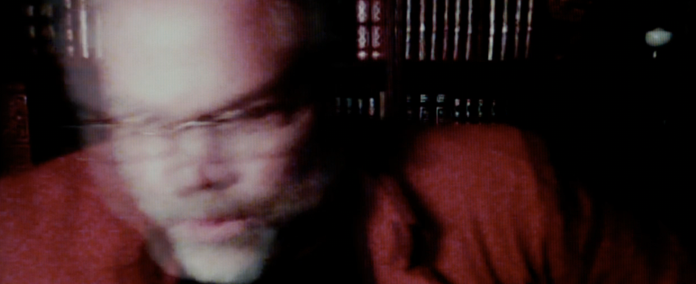 A blurred representation  of a antheral   with glasses, wearing a jacket, perchance  successful  a room  setting, arsenic  books are disposable   successful  the background