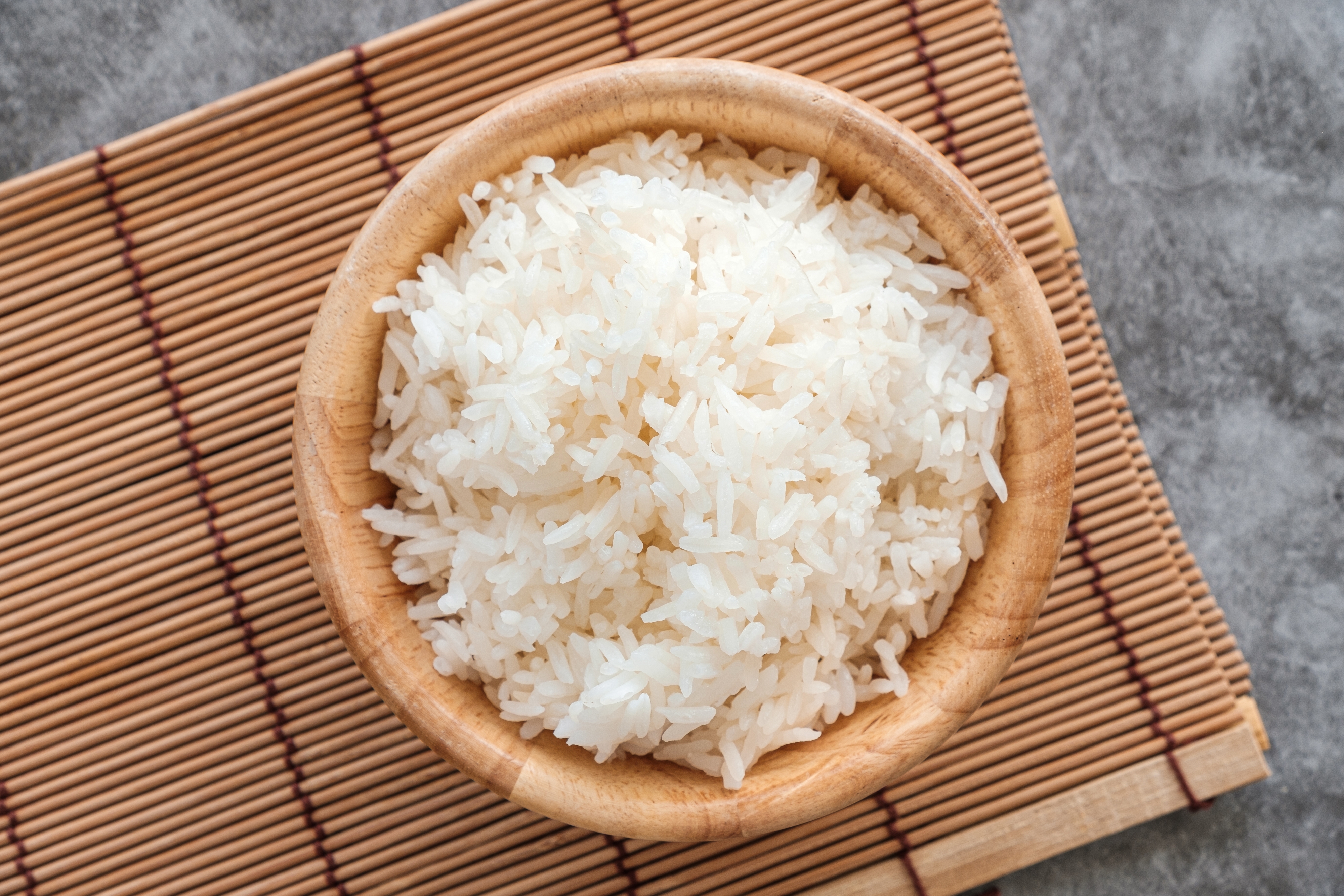 A bowl of white rice on a bamboo mat, viewed from above