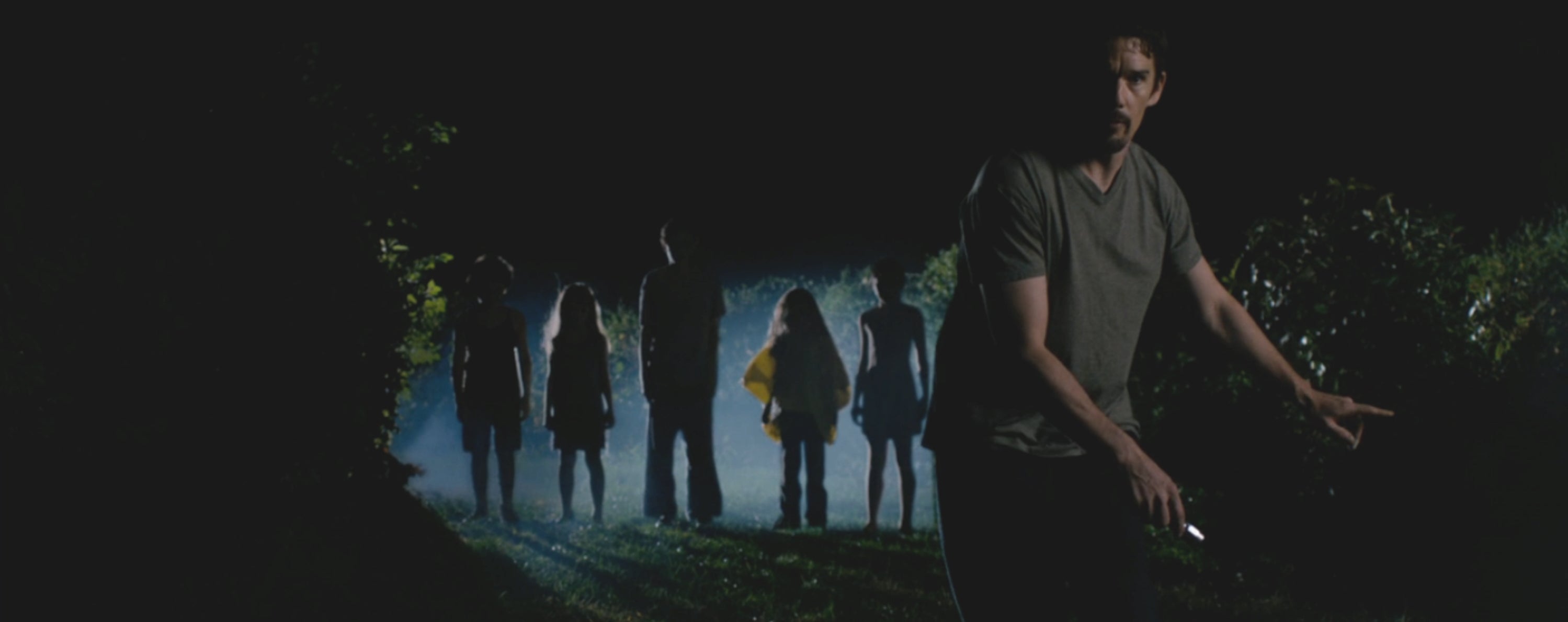 A antheral   cautiously moves with a flashlight successful  manus  portion    a radical  stands successful  the misty background, hinting astatine  a tense, mysterious scene