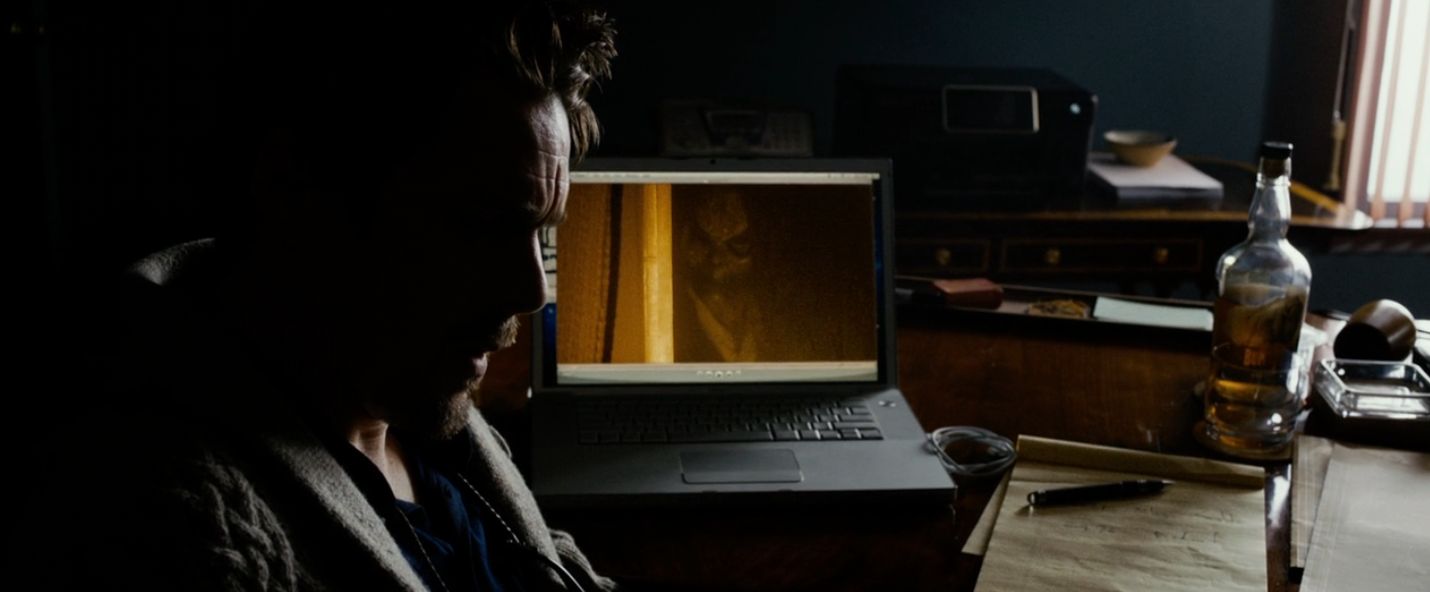 A idiosyncratic   successful  a dimly lit country   sits astatine  a table  with a laptop displaying a movie   scene, a notepad, and a vessel  nearby