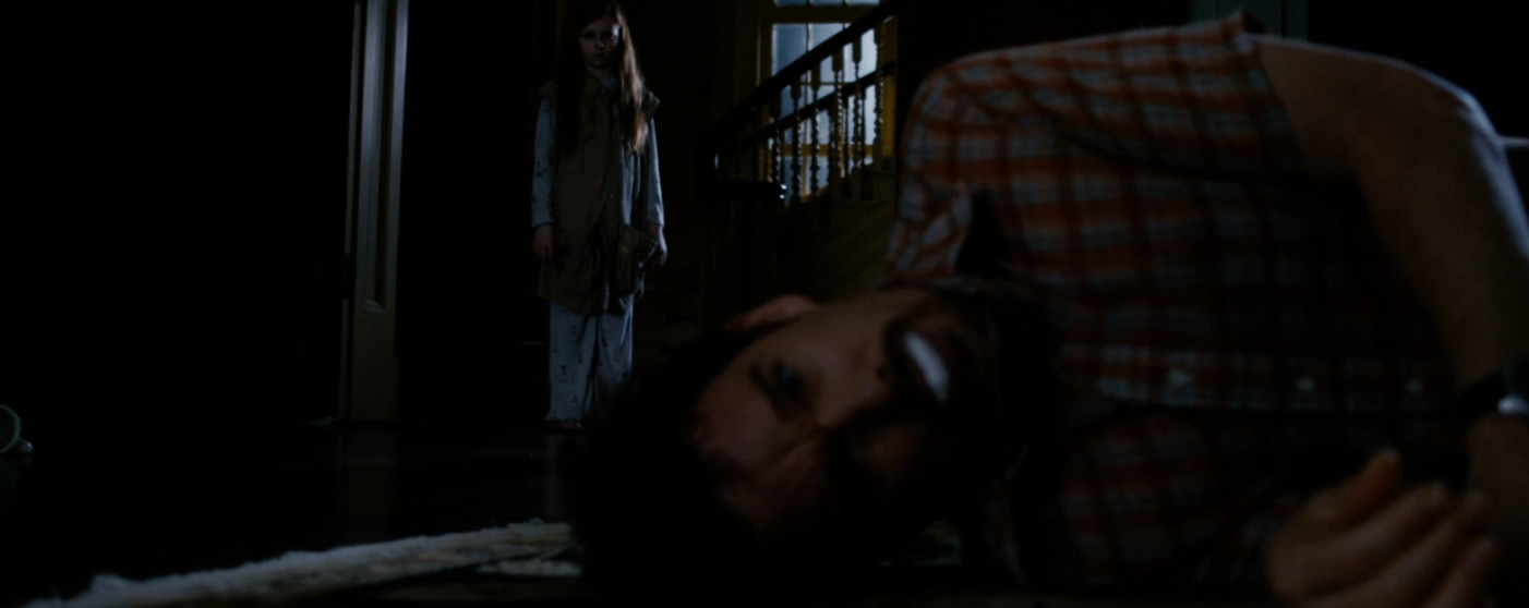 A idiosyncratic   lies connected  the floor, unfocused successful  the foreground, portion    a kid  stands successful  the inheritance  successful  a dimly lit hallway