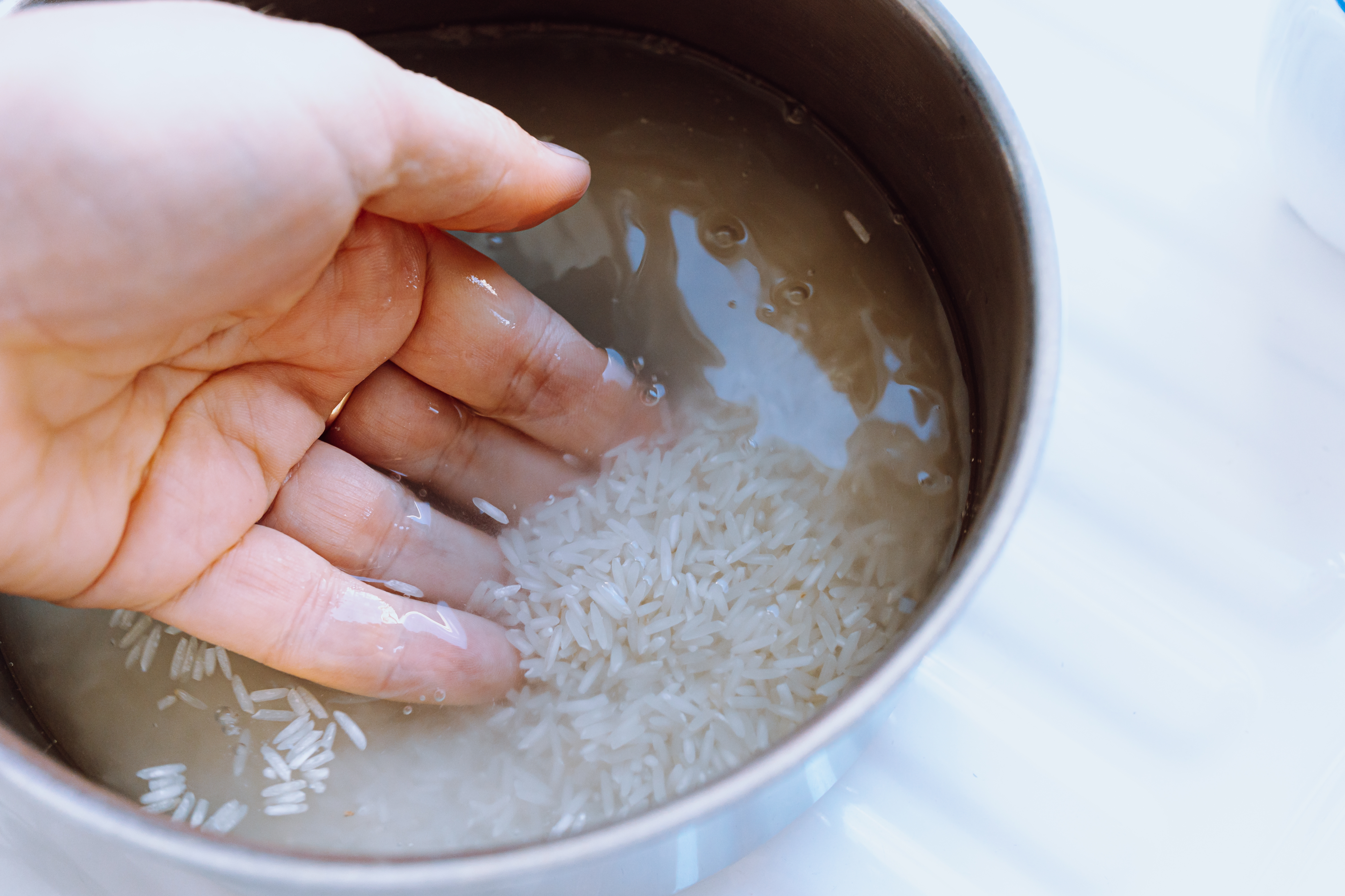 A hand rinsing uncooked rice in a metal pot filled with water