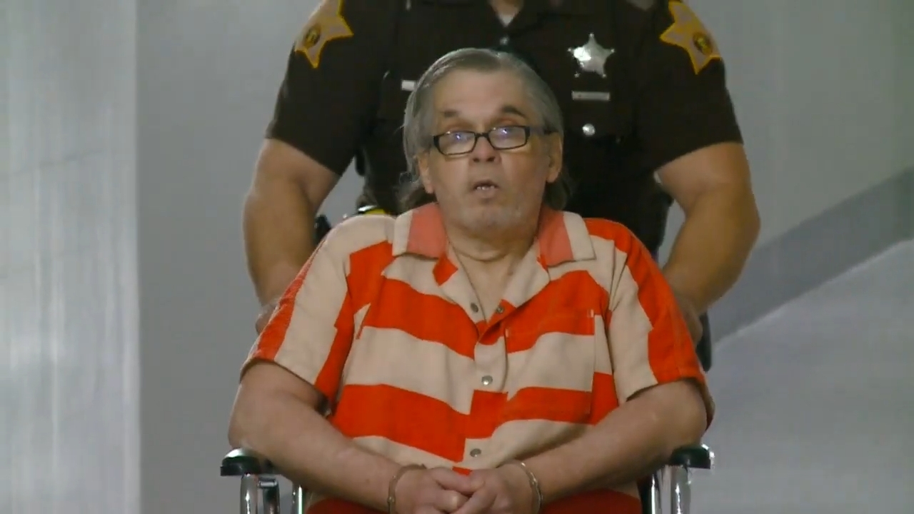 An idiosyncratic successful a striped outfit is successful a wheelchair, escorted by a uniformed officer