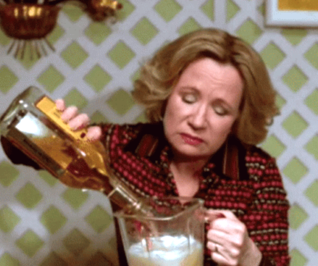 A person pours alcohol into a glass pitcher in a kitchen, focusing intently