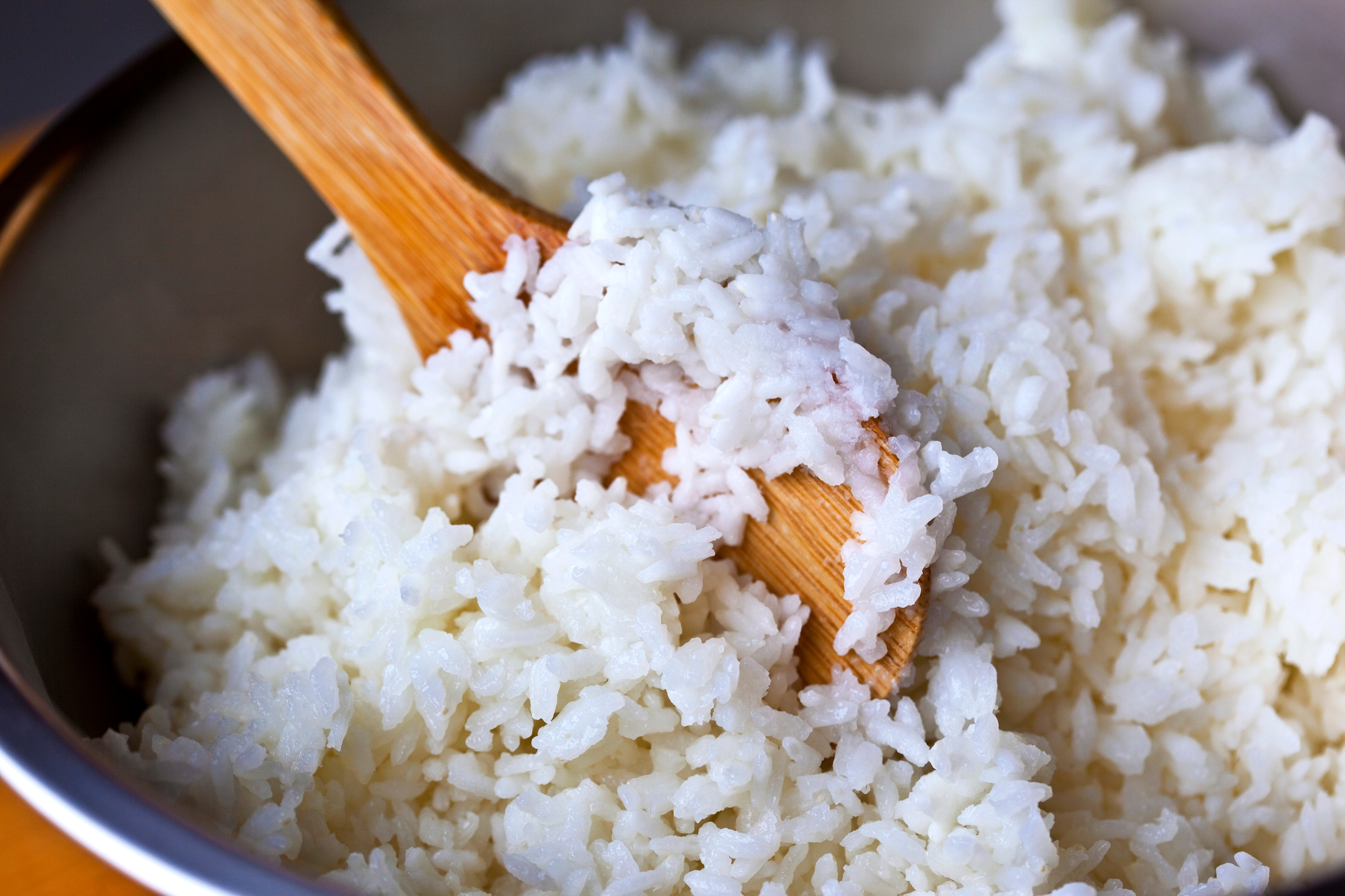 Cooked white rice in a bowl with a wooden spoon stirring through it