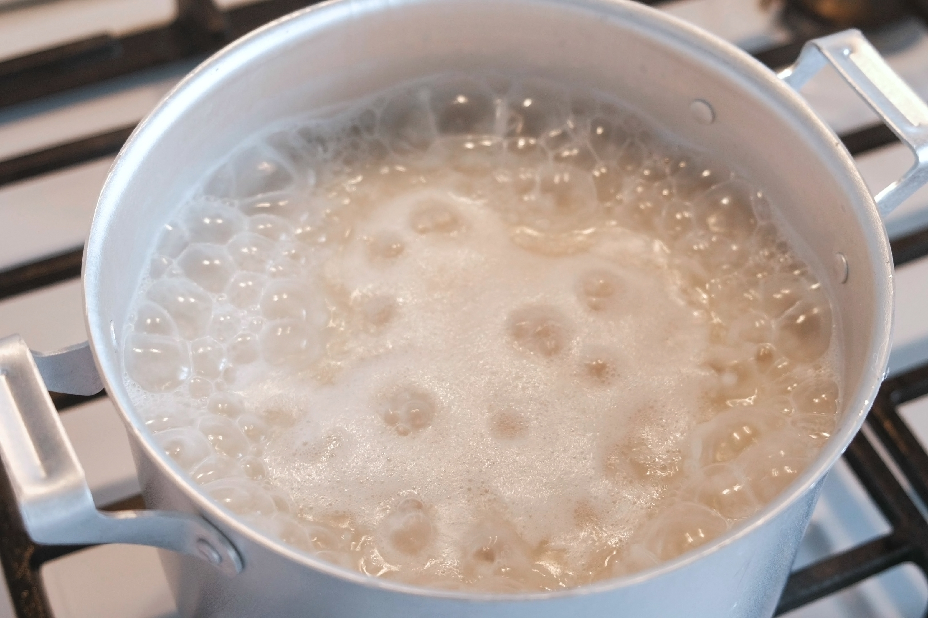 Pot of water vigorously boiling on a stove. Bubbles and steam are visible above the water surface