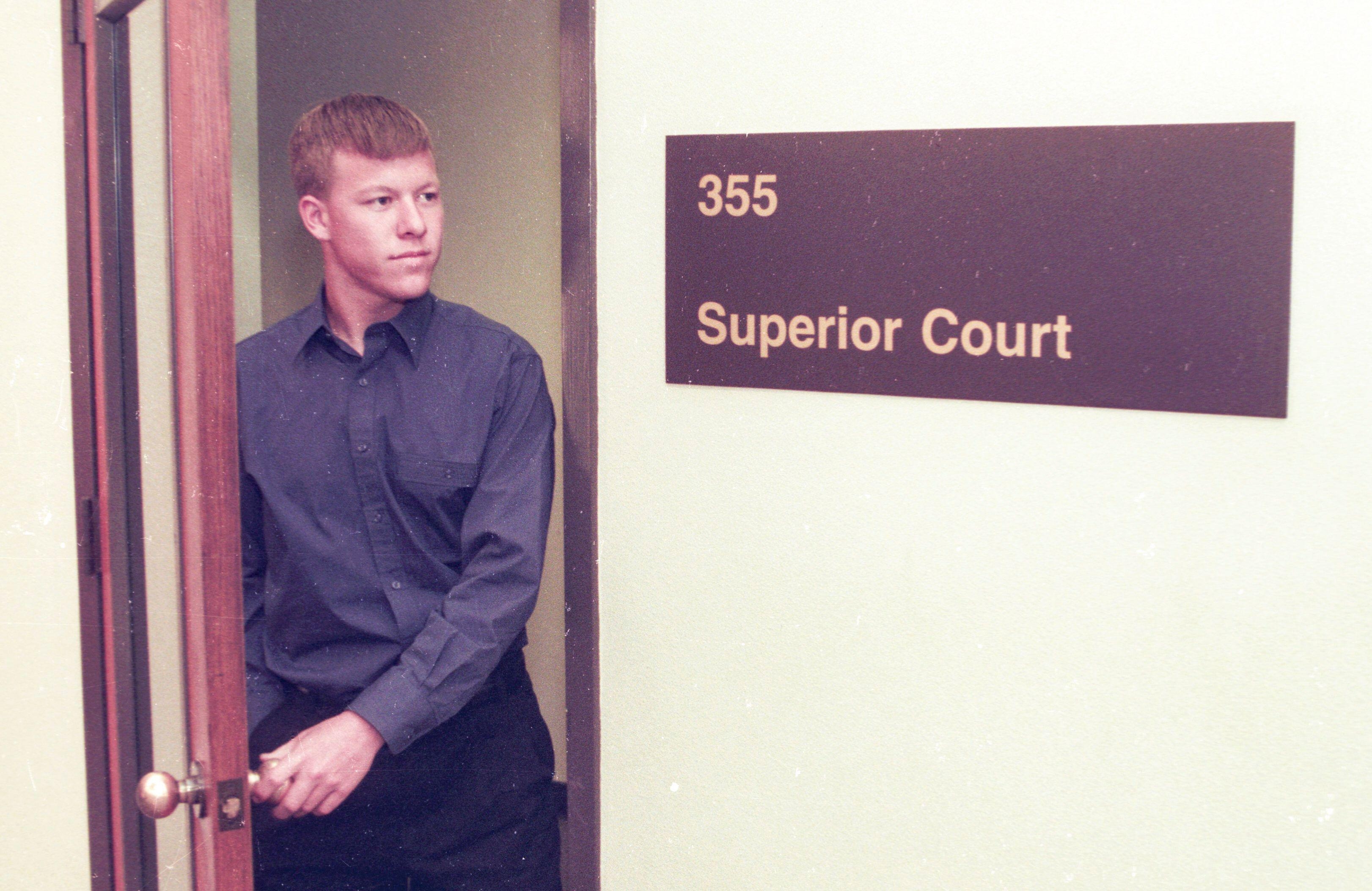 Person successful a courtroom doorway adjacent to a motion speechmaking "Superior Court 355," wearing a button-up garment and pants, looking to the side