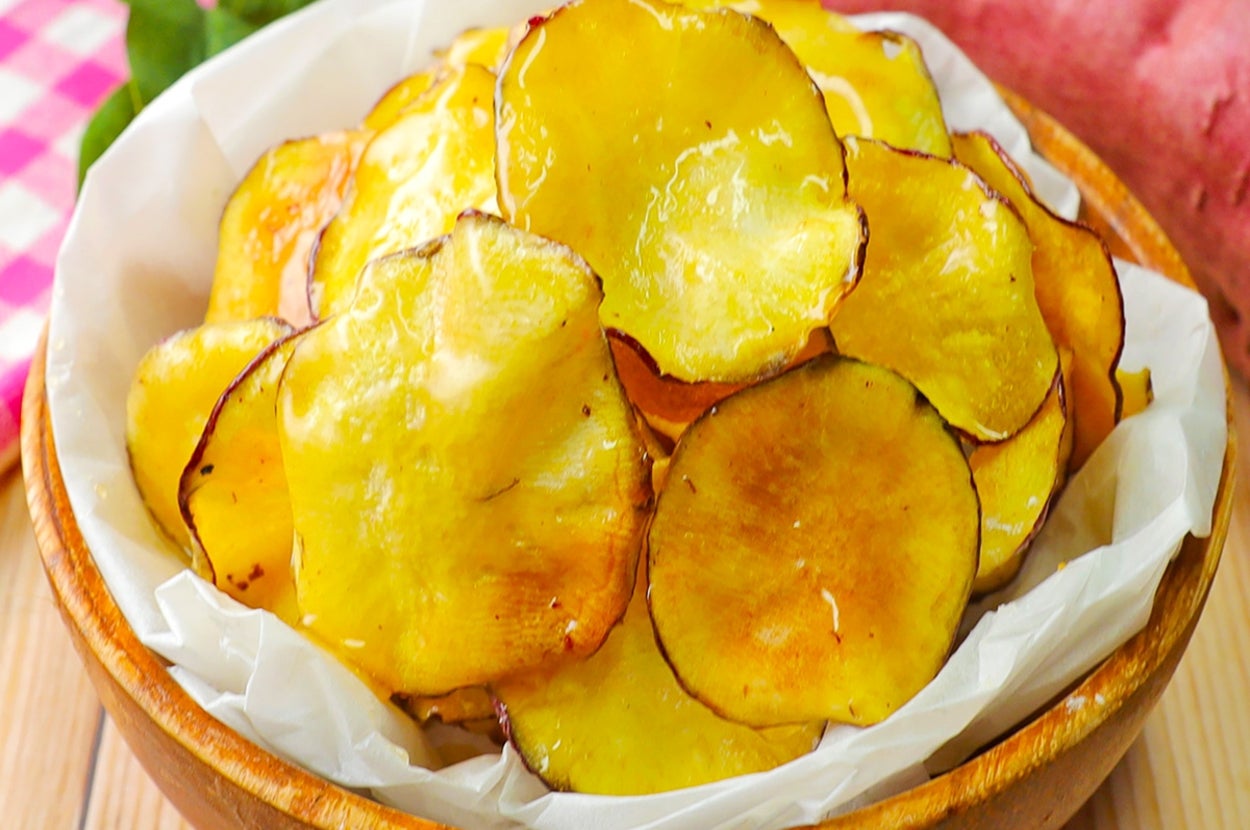 ボウルに盛られた薄切りのサツマイモチップス。後ろにサツマイモとチェック柄の布。