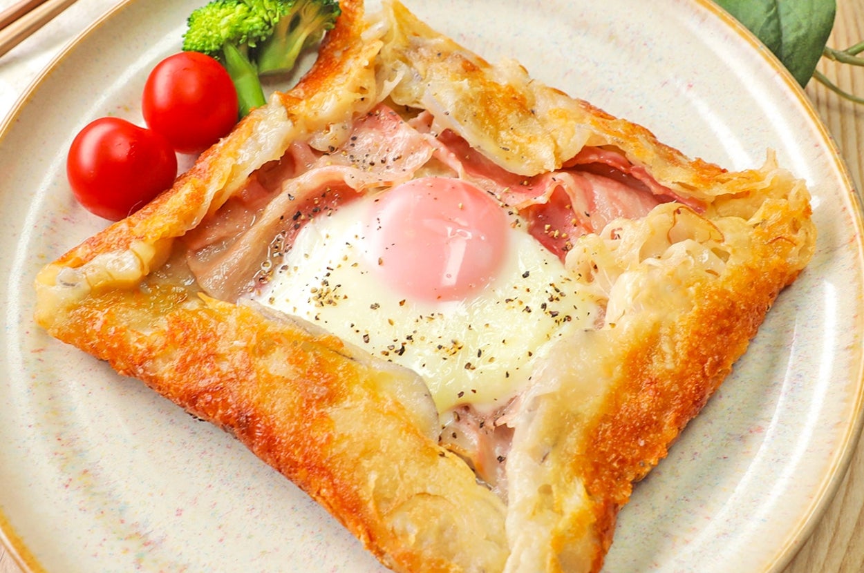 ガレットが皿に盛られており、中央には目玉焼きとベーコン、周囲にトマトとブロッコリーが添えられています。
