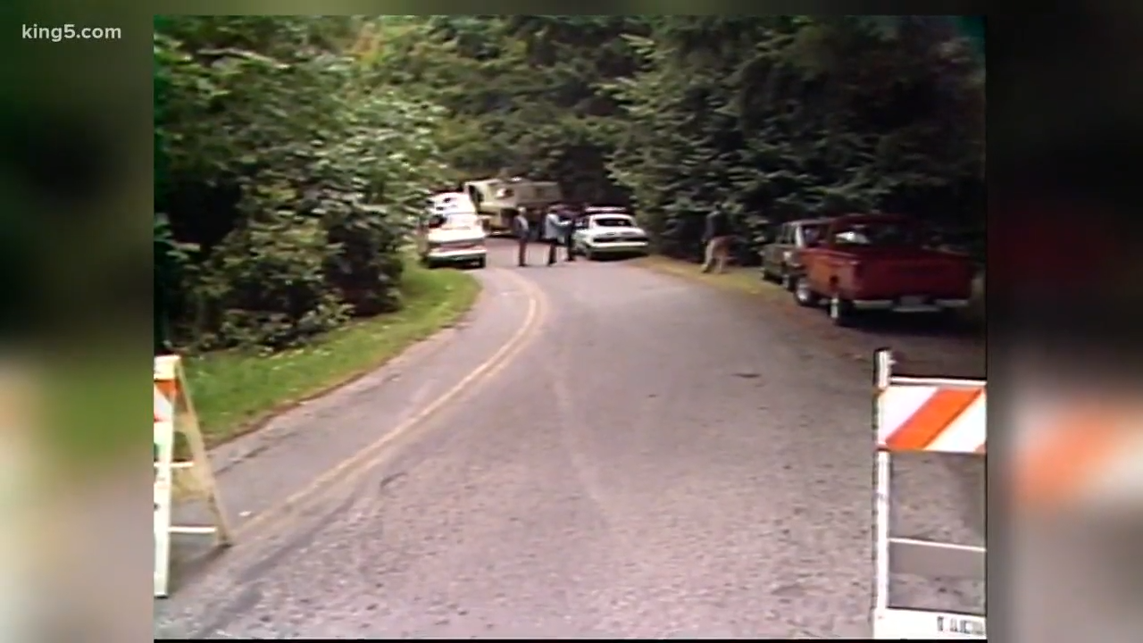 A roadworthy is partially blocked by barricades and vehicles. Three radical basal adjacent a car. Trees enactment the road