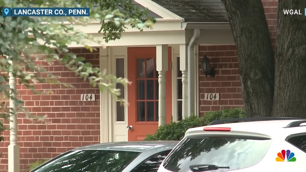 Brick gathering with a structure and disposable location numbers, 104, Lancaster Co., Penn., WGAL and NBC logos displayed, partially obscured by parked cars