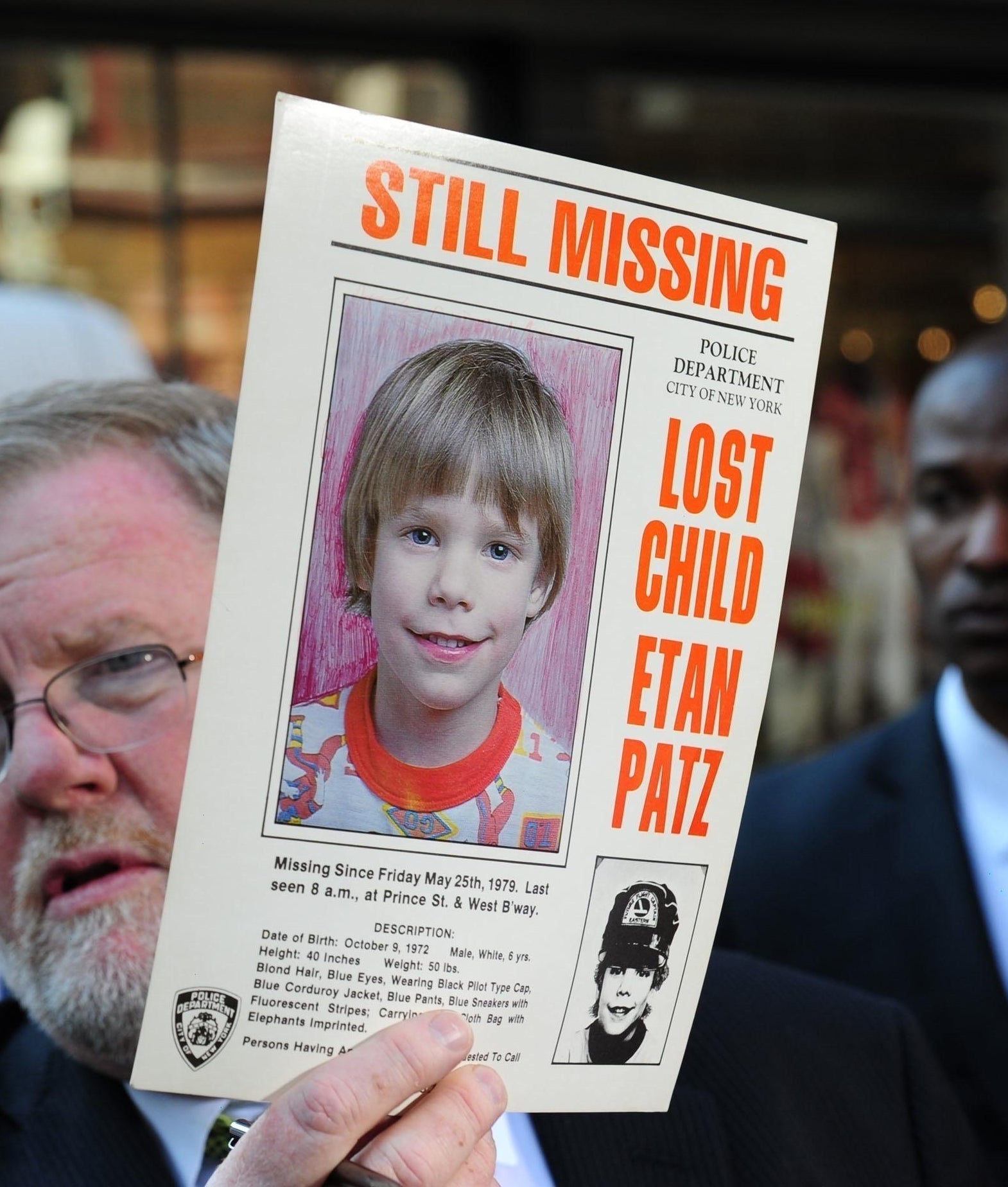A idiosyncratic holds a "Still Missing" poster for a kid named Etan Patz, with a radical of serious-looking individuals successful the background
