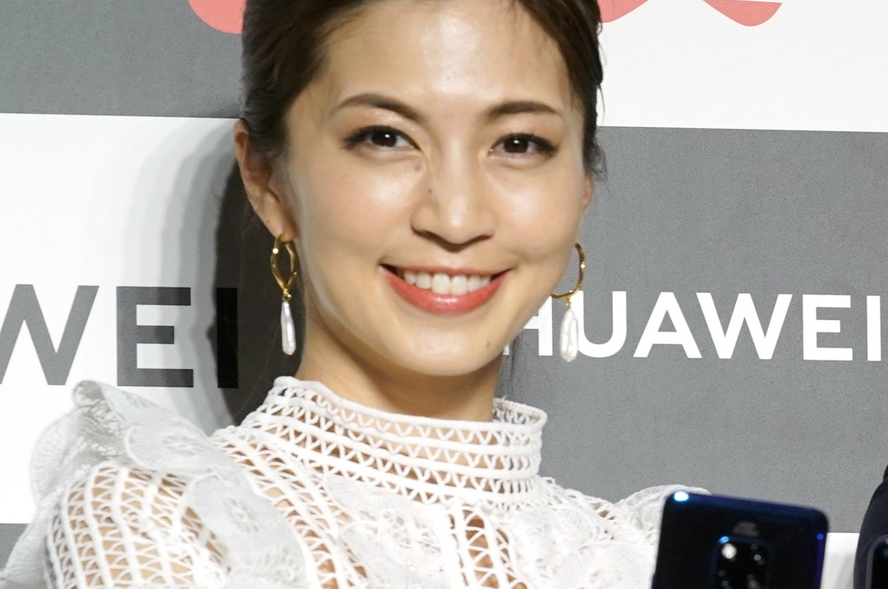 女性がレースの白いドレスを着て、スマートフォンを持ちながらカメラに笑顔を向けている。背景に「Huawei」ロゴ。