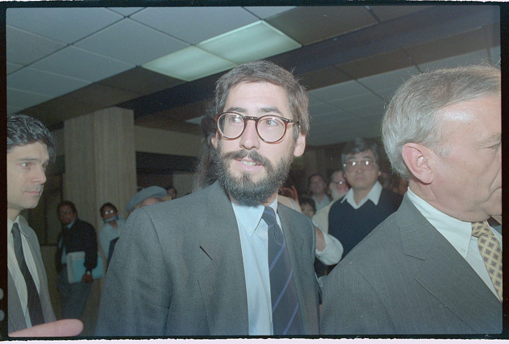 A idiosyncratic successful a suit and necktie with glasses is surrounded by a assemblage indoors