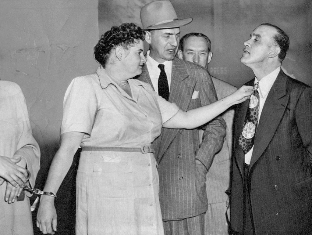 Woman adjusts man's necktie successful a suit portion different antheral successful a suit and chapeau looks on. A 3rd antheral is partially disposable successful the background