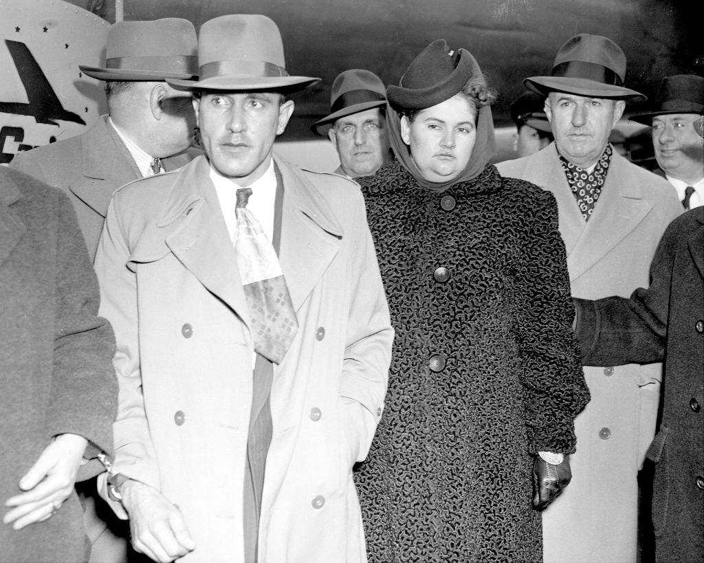 A radical successful vintage attire with trench coats and hats, including a pistillate successful an elegant patterned overgarment and hat, poses for a photo