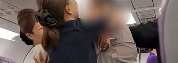 客室乗務員が男性に席を離れるよう促している航空機内の様子。