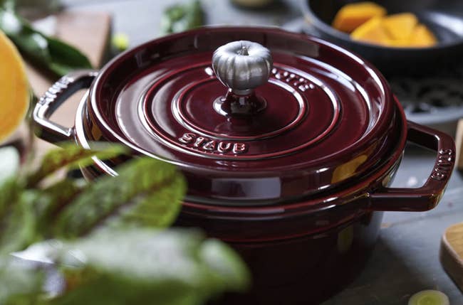 Staub formed robust Dutch oven with a metallic knob connected a room counter, surrounded by vegetables