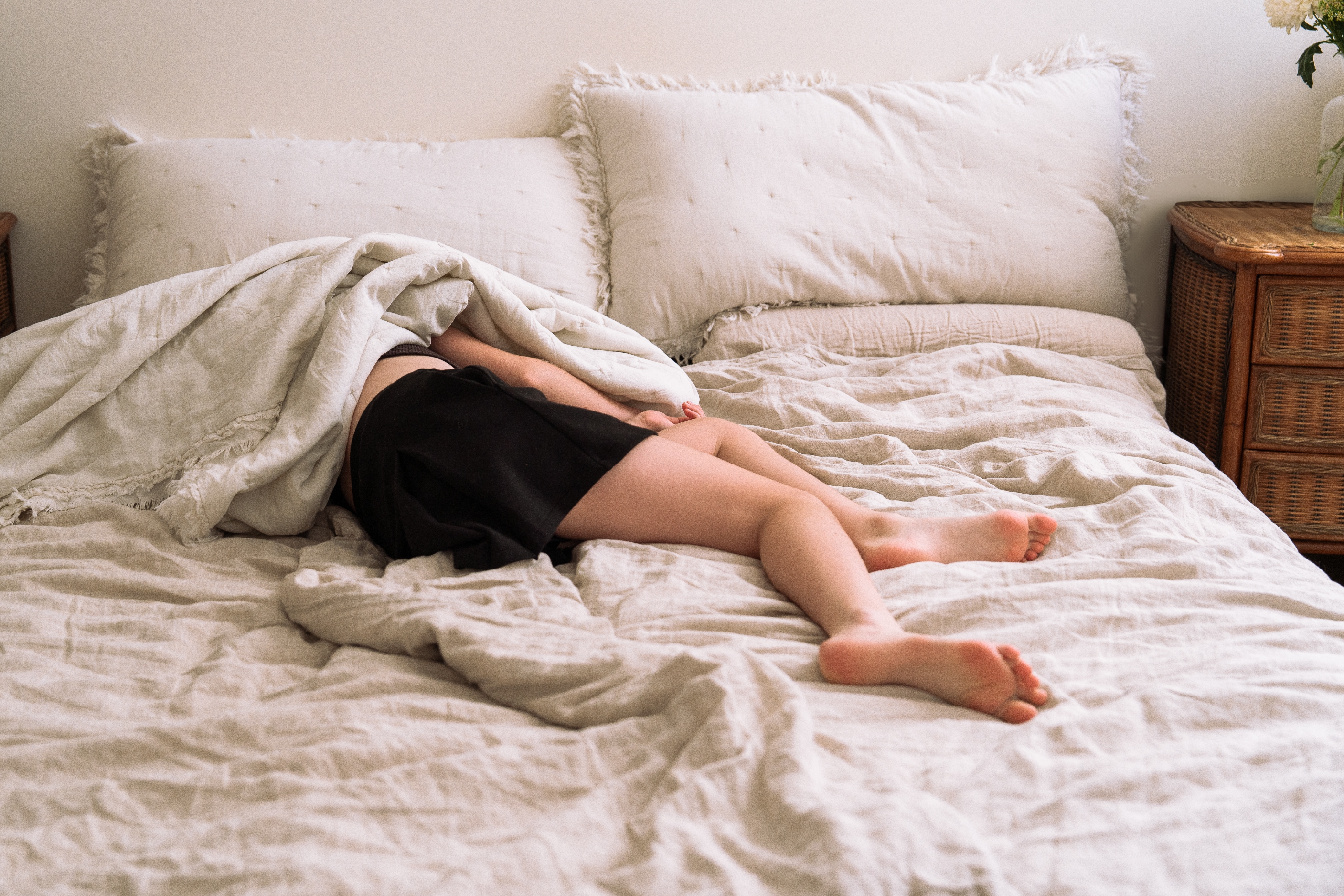 Person som ligger med ansiktet ned på en seng, delvis dekket av tepper, med synlige ben og armer