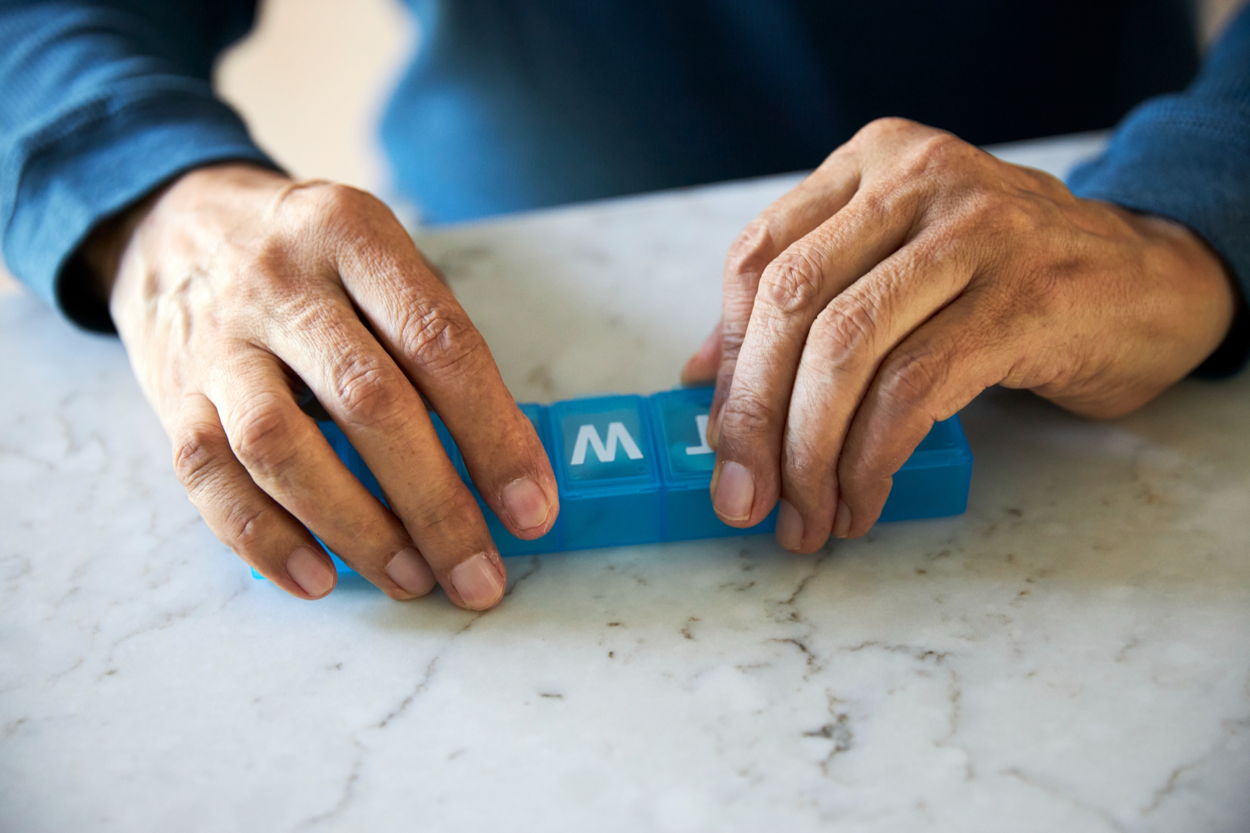 Hendene åpner en pillebeholder på en marmoroverflate