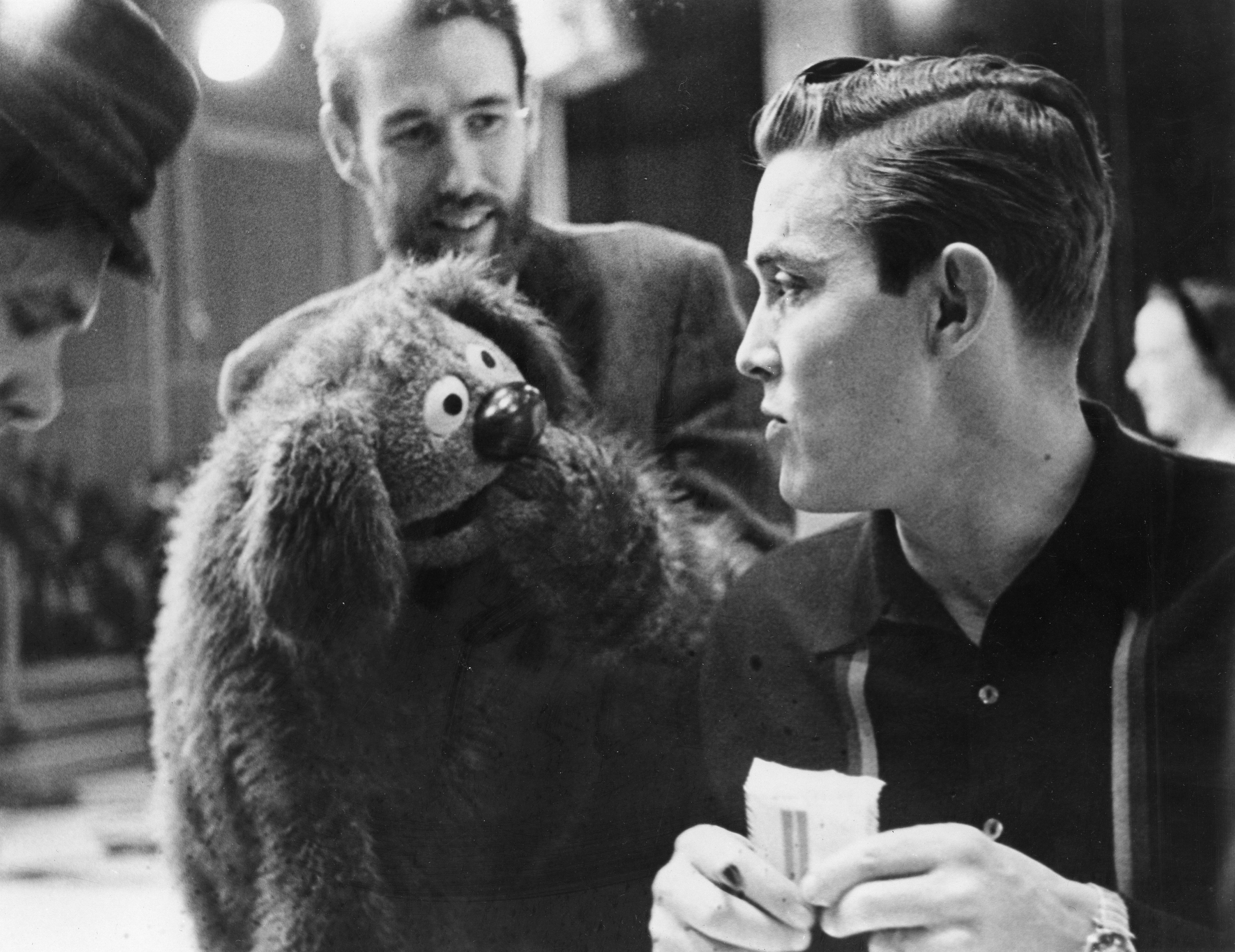 A antheral   holds a puppet resembling a shaggy dog, engaged successful  speech  with different  antheral   holding a script, apt  connected  a TV oregon  movie  set