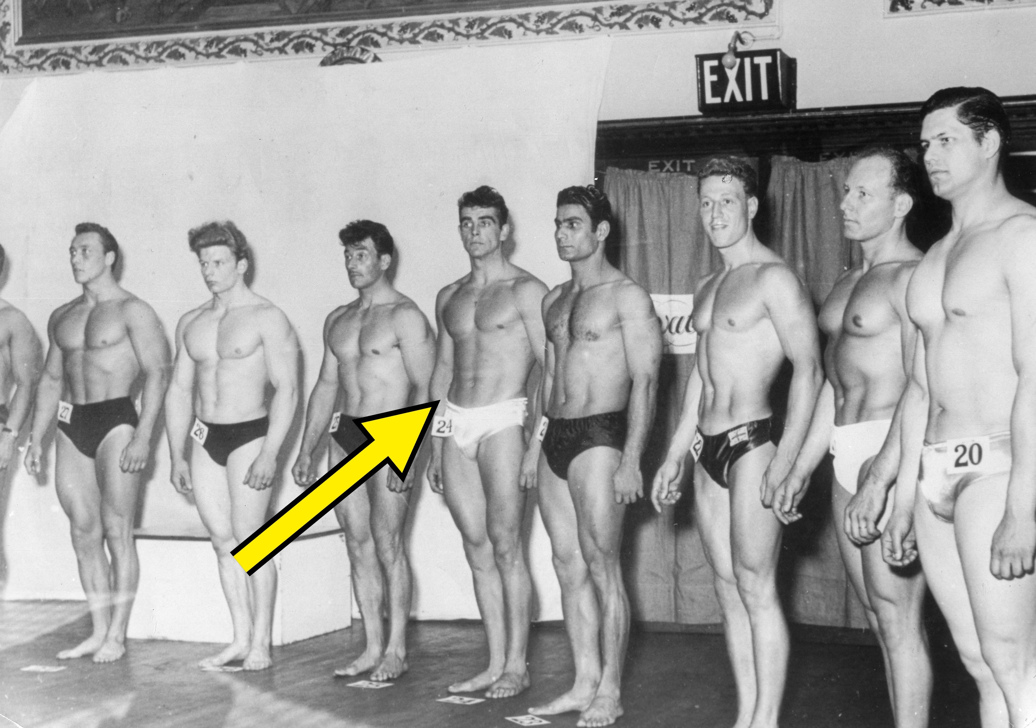 Line-up of antheral  bodybuilders connected  signifier    wearing numbered swimwear, apt  during a vintage competition