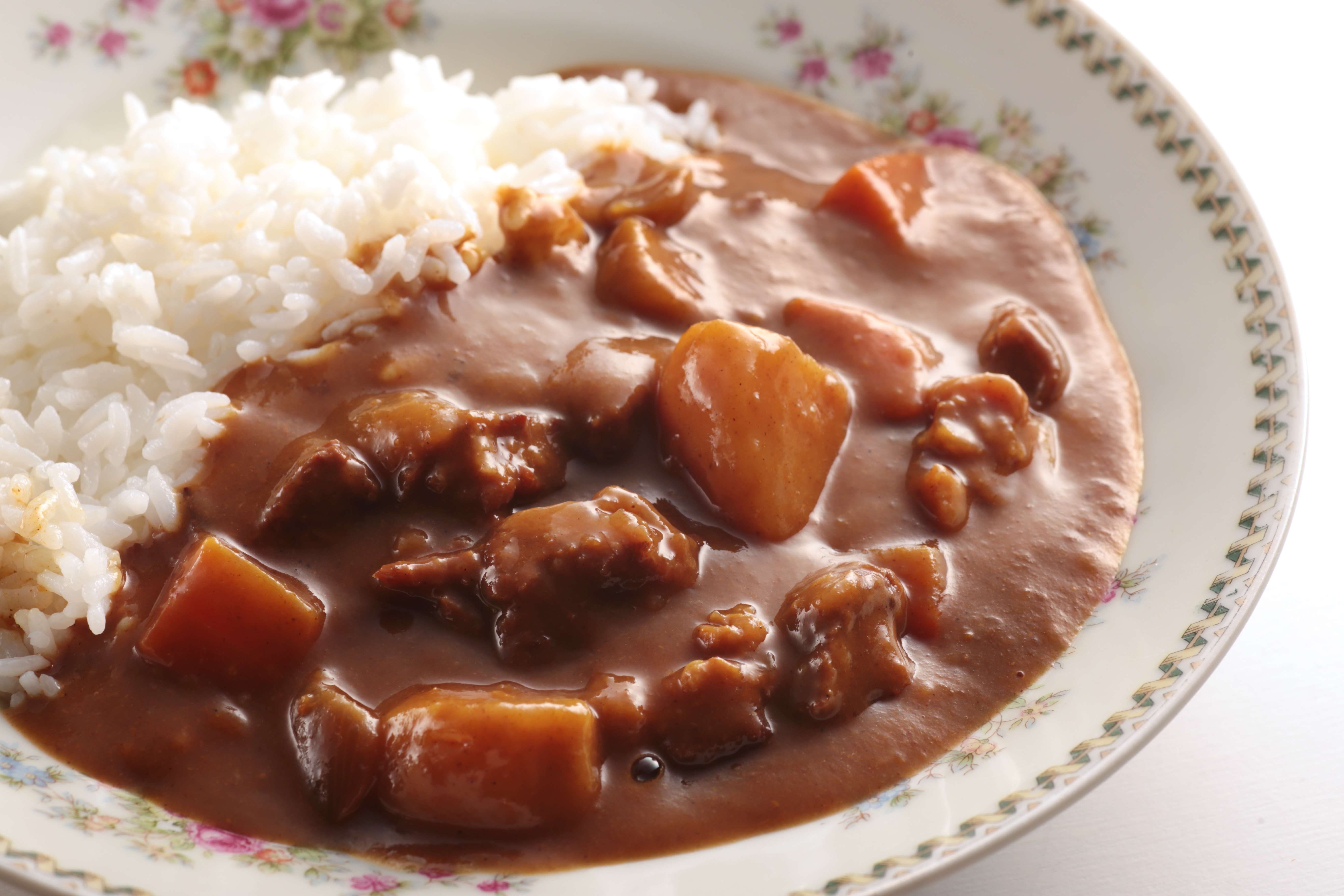A plate of rice with thick curry, featuring pieces of meat and vegetables in a creamy sauce, served on a floral-patterned dish
