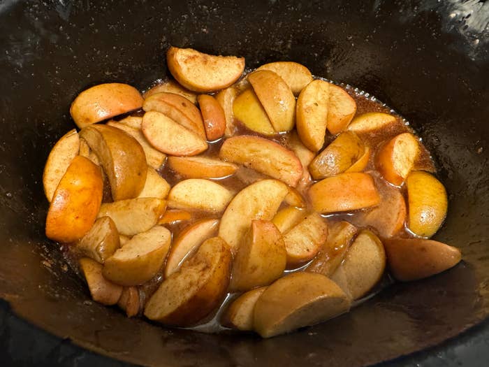 Sliced apples in a slow cooker with cinnamon and spices, partially cooked in a sweet sauce