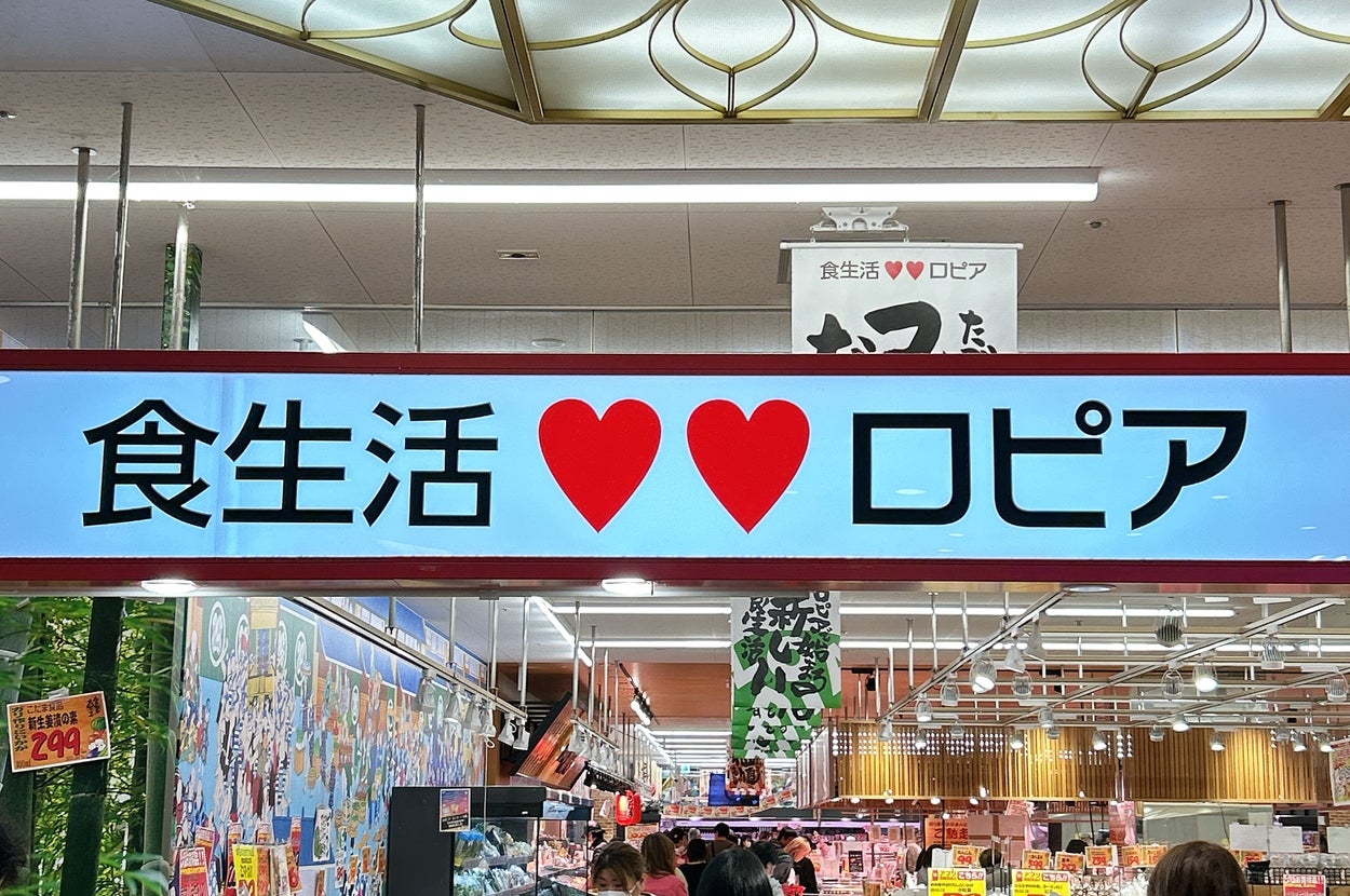 スーパーの店内風景。看板に「食生活♥♥ロピア」と表示。お客さんが商品を見ている様子。