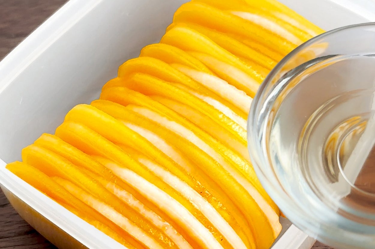 プラスチック容器に並べられた薄切りのかぼちゃに、液体が注がれている様子。