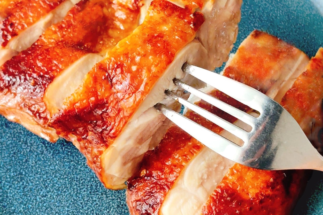 フォークで切られたローストチキンの大きな切り身が青い皿にのっている。