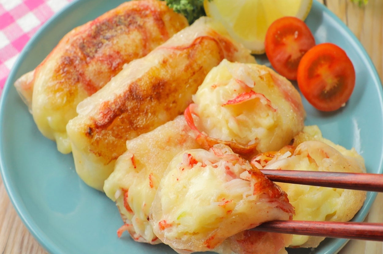 餃子の盛り付け。皿には切ったレモンやトマト、緑の葉も添えられている。箸で一つの餃子を取っている場面。