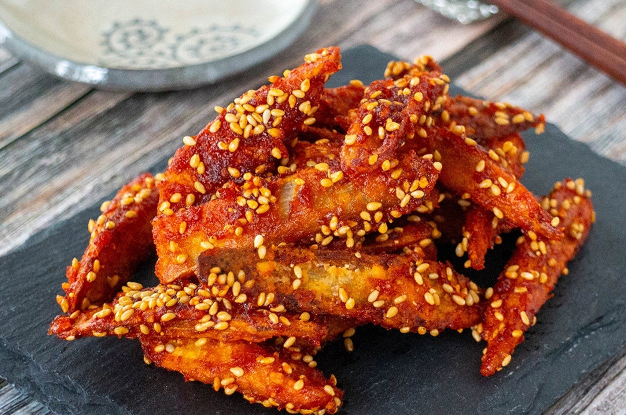 ゴマをまぶしたスパイシーな手羽先が石のプレートに盛り付けられている様子。後ろに箸と小皿。