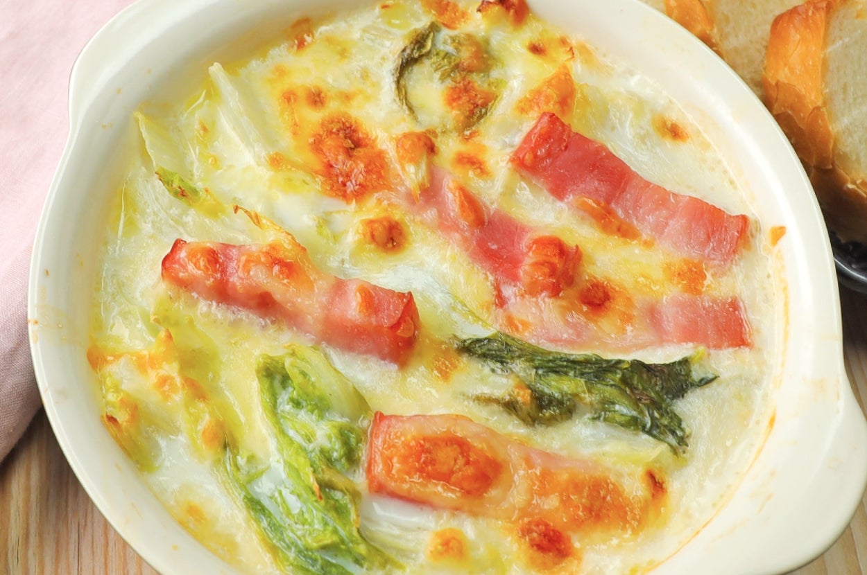 グラタン皿に入った焼きたてのクリーミーなグラタン、ベーコンと野菜がトッピングされている。隣にパンがある。