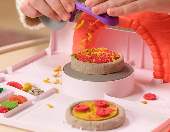 Hands shaping artifact pizza with mold successful a playset, featuring unreal toppings and room accessories. Ideal for children's imaginative play
