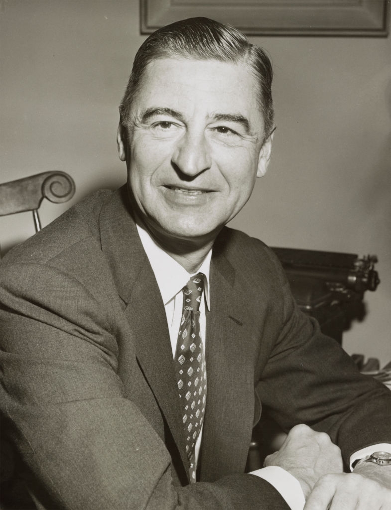 Person successful a suit seated, smiling and looking somewhat off-camera