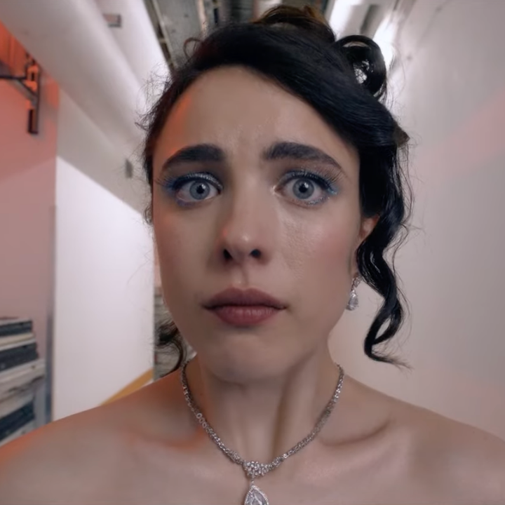 A woman with an updo looks surprised in an industrial hallway, wearing a strapless dress and a necklace