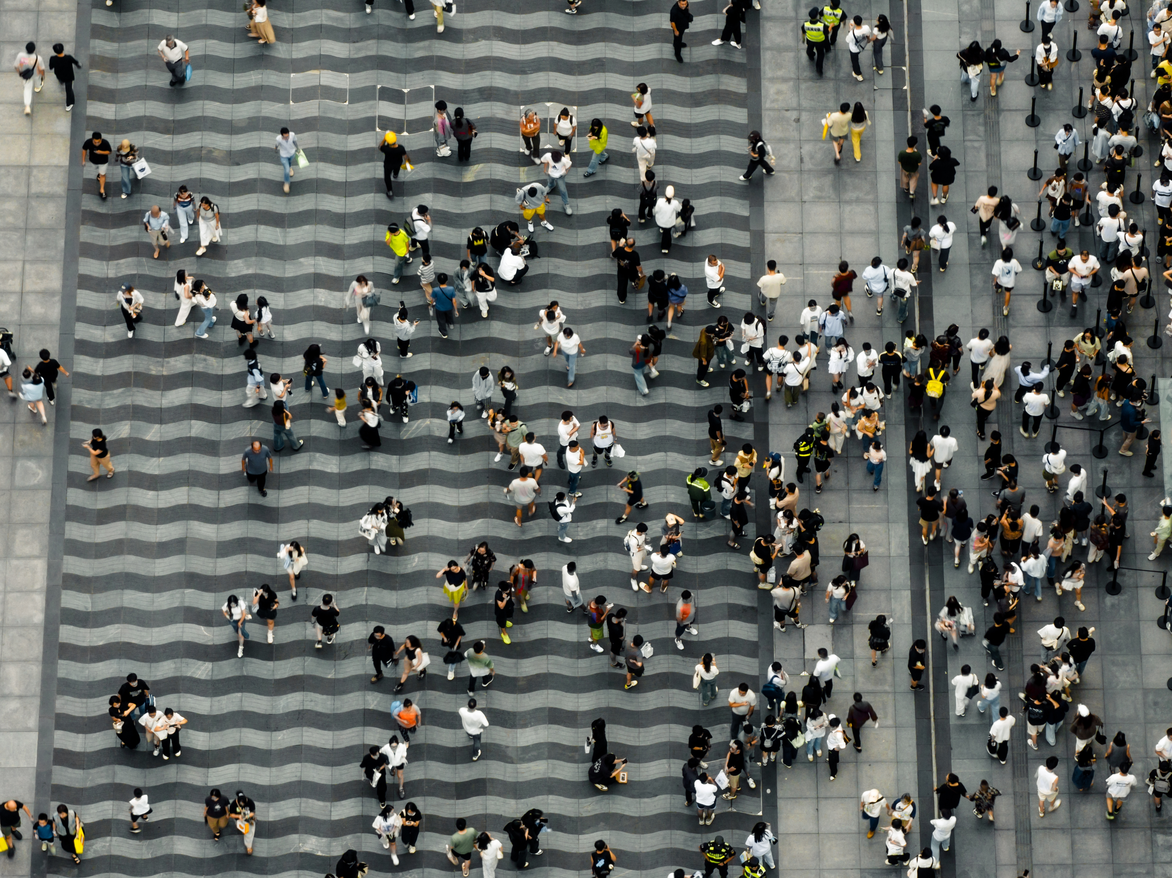 Aerial view of a crowded public space with people walking in various directions on a wavy-patterned surface