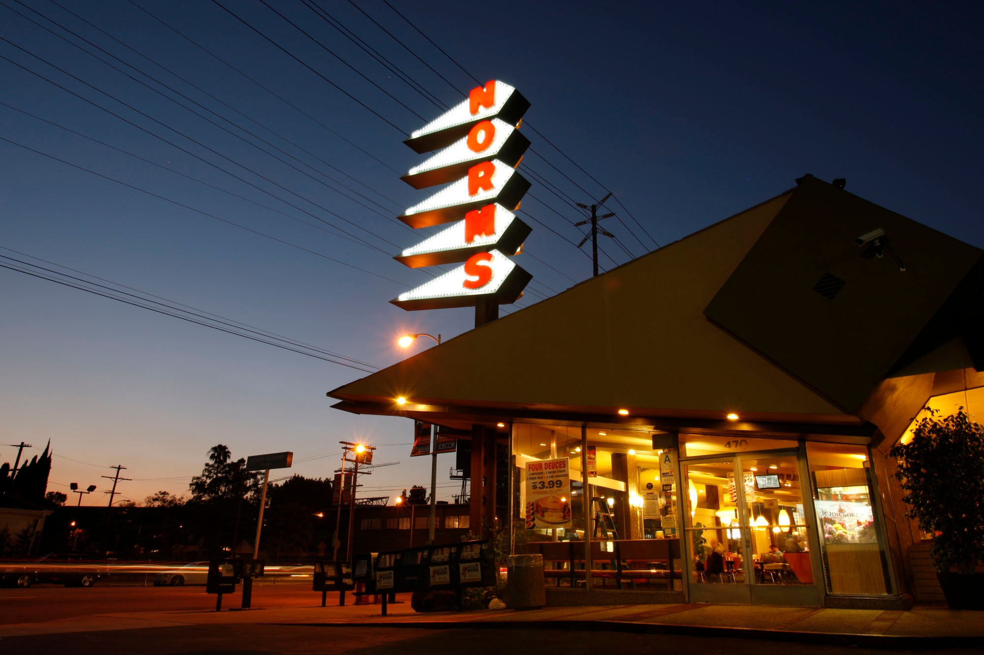 Norms restaurant at dusk with illuminated signage. Seen from the outside, warm lights glow inside, indicating it's open and welcoming to customers