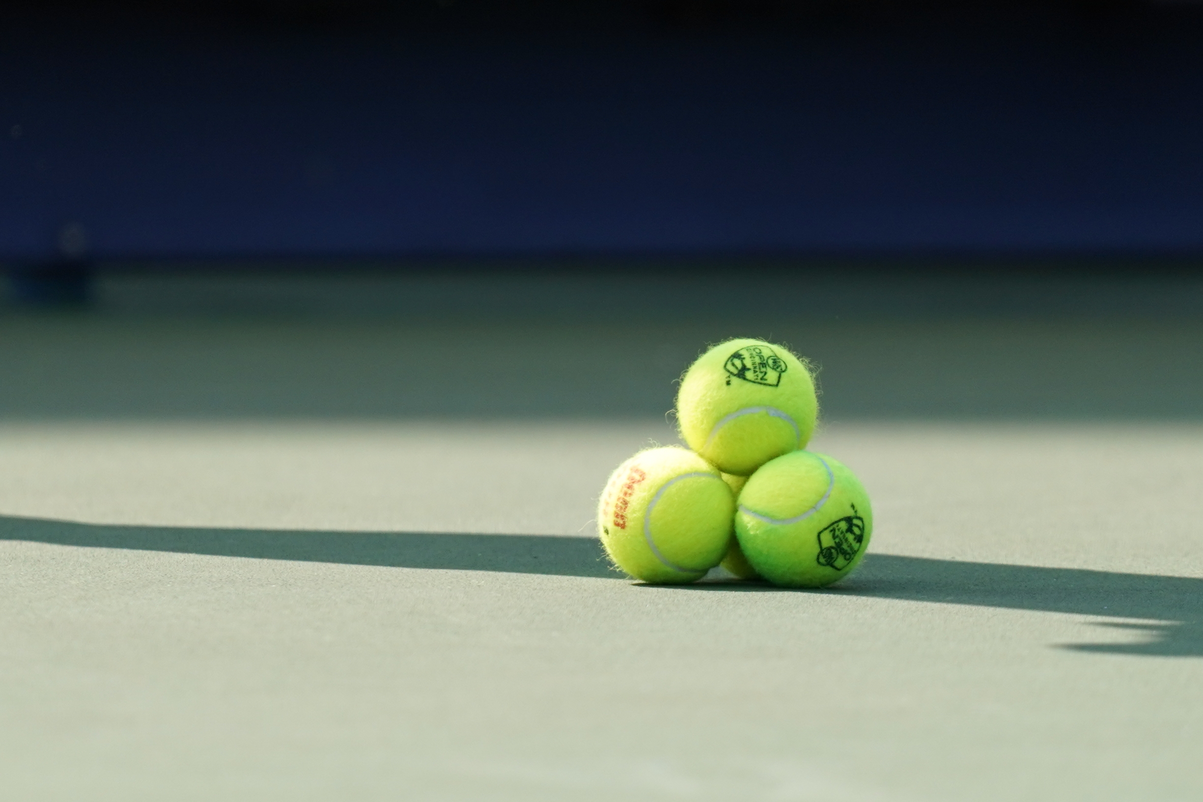 Three tennis balls stacked in a triangular formation on a tennis court surface