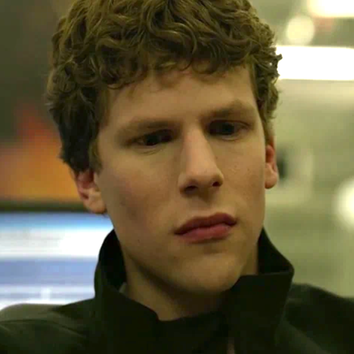 Person with curly hair looks thoughtful, wearing a dark jacket, in a focused setting
