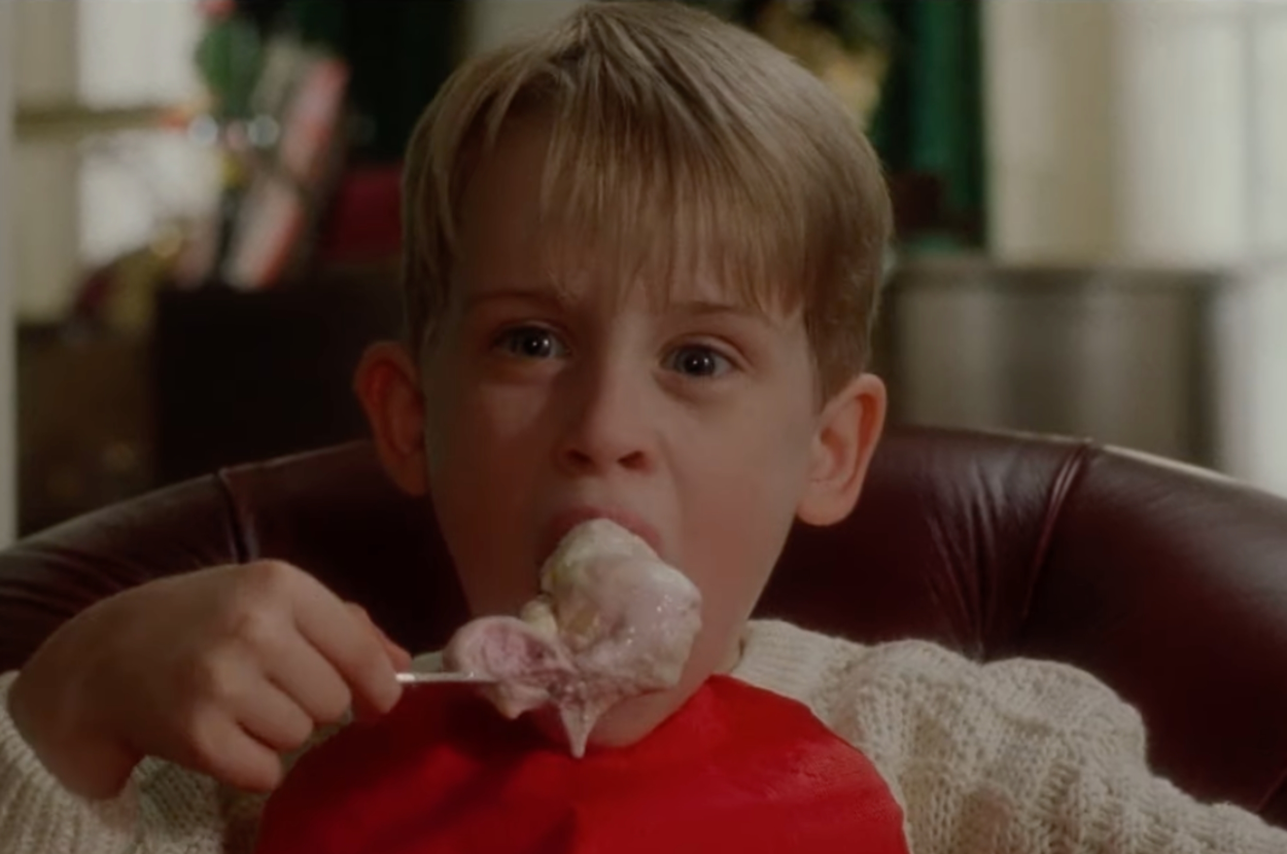 Child in a sweater enjoys ice cream from a spoon, looking directly at the viewer with a focused expression