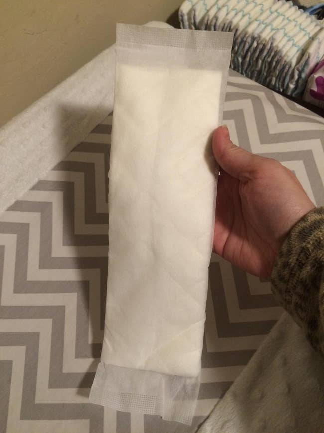 A manus holds a ample diaper pad implicit a patterned surface, with diapers successful the background