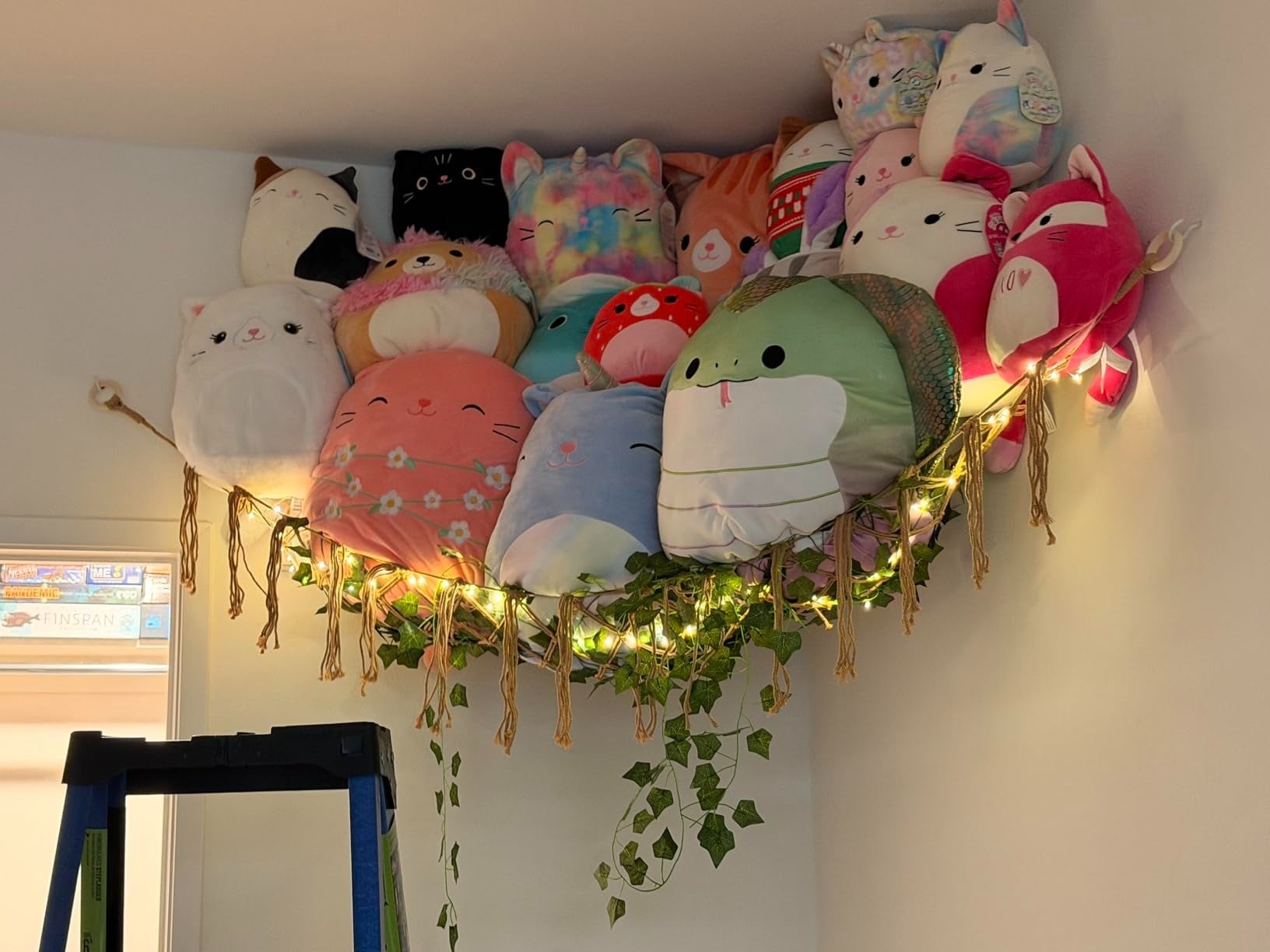 Plush stuffed animals are displayed supra  a doorway connected  a hammock with drawstring  lights and hanging ivy for decorative location  storage